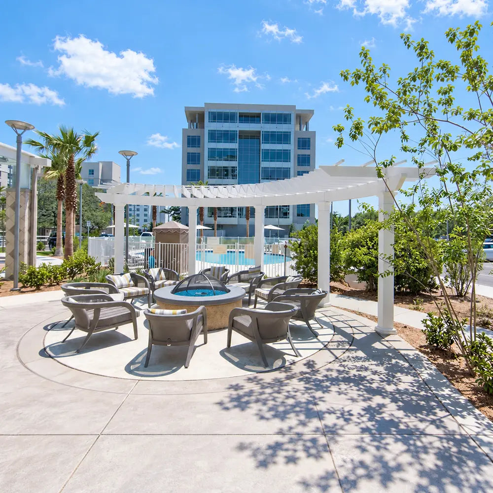 White Structureworks Trex Pergola covering lounge chairs arranged around a circular fire feature beside a fenced swimming pool.