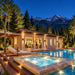 The illuminated Banff one-bedroom suite on a bright Colorado summer night, with adults watching sports on television through the glass doors and the pool and spa glowing beneath the Rocky Mountains.