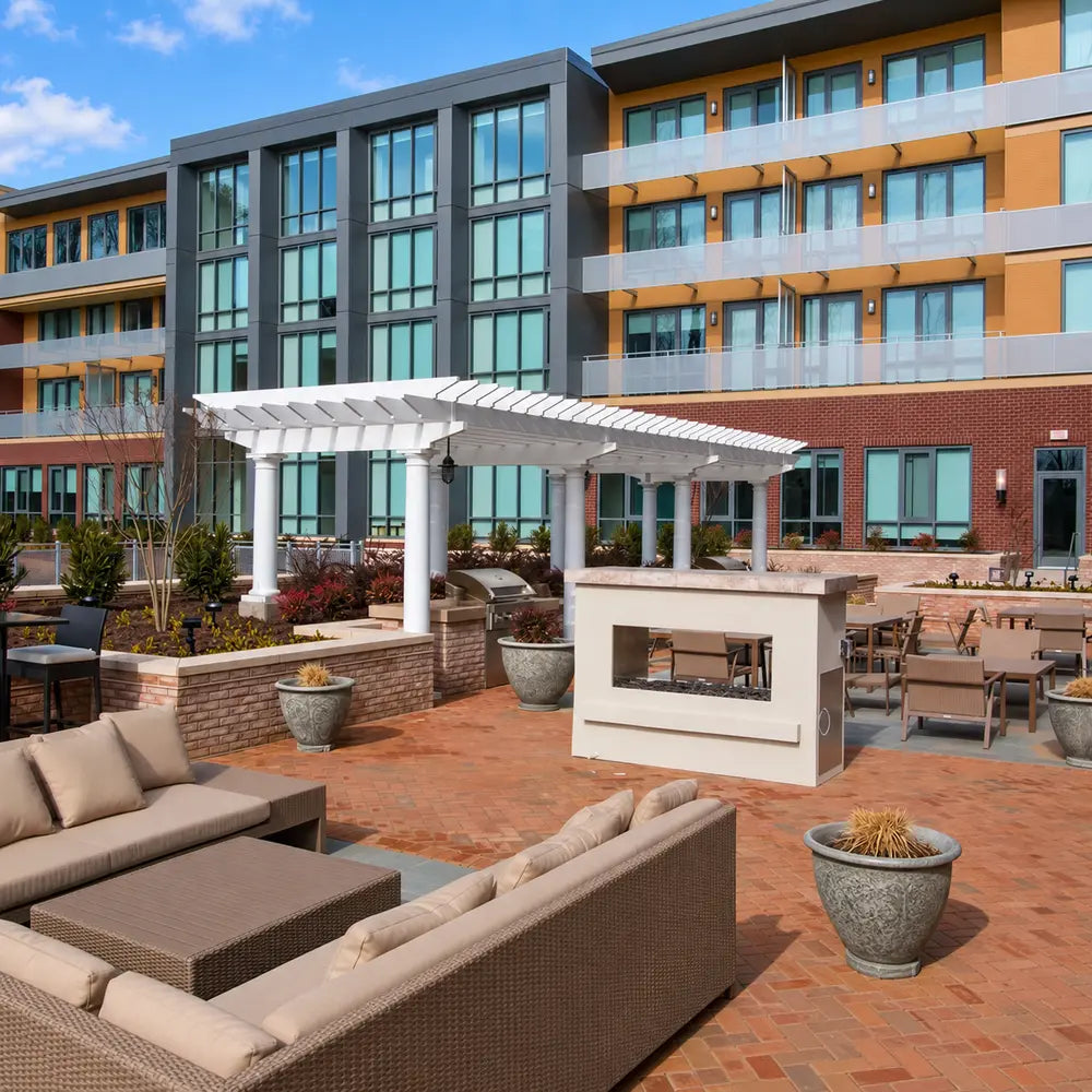 White Structureworks Trex Pergola in a landscaped apartment courtyard with grills, lounge seating, dining tables, and a modern fire feature.