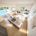 Elevated view inside the Banff Garden Suites showing a white sectional sofa, marble kitchen island, open-plan layout, and private pool beyond the windows.