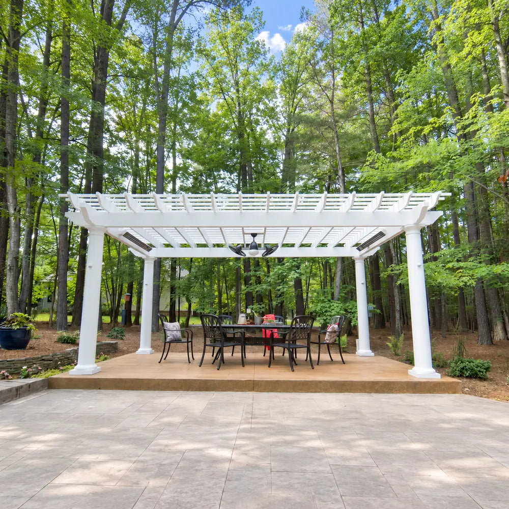 Centered white Structureworks Trex Pergola with built-in lighting, a ceiling fan, and a black dining set in a wooded patio setting.