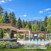 The Algonquin Multi-Room Freedom House presented as a private Colorado mini resort, featuring a turquoise pool, four cascading spillways, covered outdoor kitchen, fireplace pavilion, and vibrant green native trees.