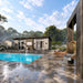 Side view of the Muskoka Garden Suites beside a pool with fountain jets, a hanging chair, lounge seating, trees, and a peaceful landscaped setting.