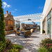 White Structureworks Trex Pergola with ceiling fans covering elegant patio seating beside a stone fireplace and outdoor kitchen.