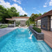 Algonquin Garden Suites outdoor area with a modern turquoise pool, cascading wall fountains, stone architecture, lounge chairs, landscaped greenery, and a shaded fireplace pavilion.