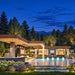 The Algonquin Multi-Room Freedom House illuminated on a clear Colorado summer night, with a glowing pool, cascading water features, pavilion lighting, fireplace, and Rocky Mountain scenery.