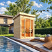 TS TwoSauna with a smooth light-wood exterior and glowing glass entrance beside a calm pool, curved wooden loungers, folded towels, and lush landscaping.