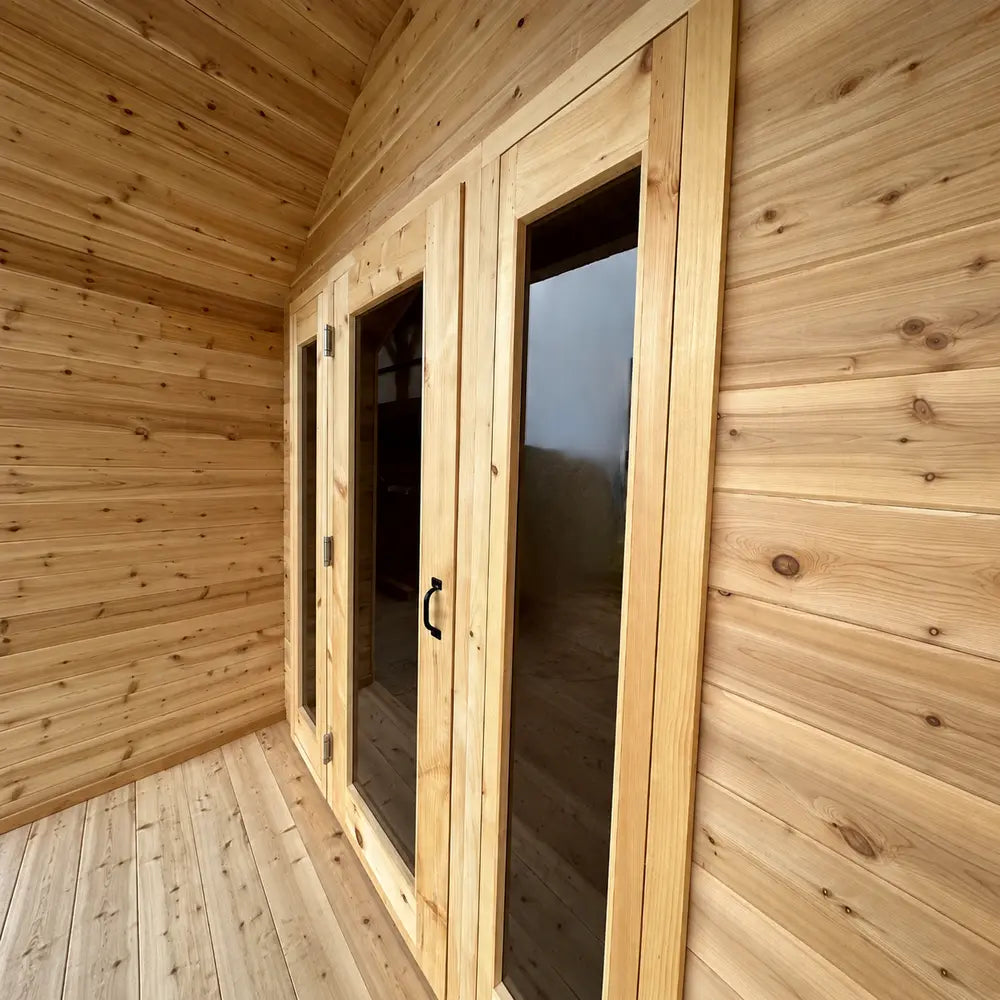 Wooden entrance of the Sawmill Structures CabinSauna featuring tall glass panels, natural wood framing, and a black door handle.