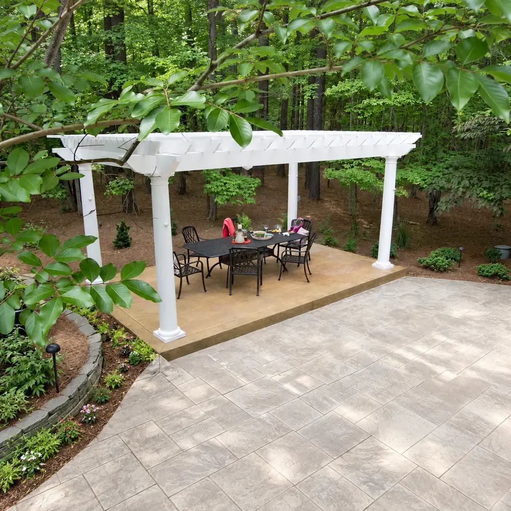 White Structureworks Trex Pergola sheltering a black dining table and chairs on a secluded patio surrounded by dense woodland.