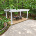 White Structureworks Trex Pergola sheltering a black dining table and chairs on a secluded patio surrounded by dense woodland.