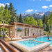 The Banff one-bedroom poolside suite on a sunny Colorado day, with one adult swimming, another sitting beside the pool, and a third reading on a chaise beneath green trees and Rocky Mountain views.