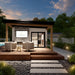 Tremblant Garden Suites glowing warmly at dusk with a covered wood patio, wicker chairs, stone accent wall, linear fire pit, and illuminated garden path.