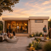 Rectangular light wood cabin with glass doors, outdoor patio, and people socializing at sunset.
