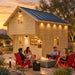 Front three-quarter view of the Freedom Loft Studio Jumbo Grand 130 SD at golden hour. Four adults socialize around a fire feature while the compact backyard bar glows through the windows amid upscale Nevada desert landscaping.
