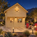 Front view of the illuminated Freedom Loft Studio Jumbo Grand 130 SD during a clear Nevada night. Family and friends watch sports inside while pathway lights, red patio chairs, desert plants, boulders, and distant mountains frame the structure.
