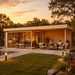Rectangular wood studio with glass doors, a patio lounge, and an indoor bar area at sunset by a pool.