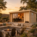 Rectangular wood studio with glass sliding doors, stone patio, fire pit, and outdoor seating at sunset.