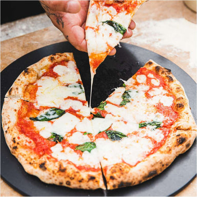 Gozney 14" Pizza Server with a hand lifting a slice from a margherita pizza resting on the round charcoal surface.
