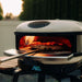 Gozney Arc Pizza Oven Mantel fitted at the mouth of a Bone Arc oven with a pizza on a peel going in and the display reading 865.