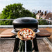 Gozney Arc Pizza Oven Mantel on an Off-Black Arc oven on a rooftop with a finished pizza held on a peel in front and a city skyline behind.