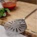 Gozney Balance Turning Peel close view of the perforated head resting on a wooden board with a bowl of tomato sauce and basil behind.