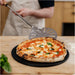 Gozney Balance Turning Peel held by a person in an apron above a finished margherita pizza on a black pan on a kitchen counter.