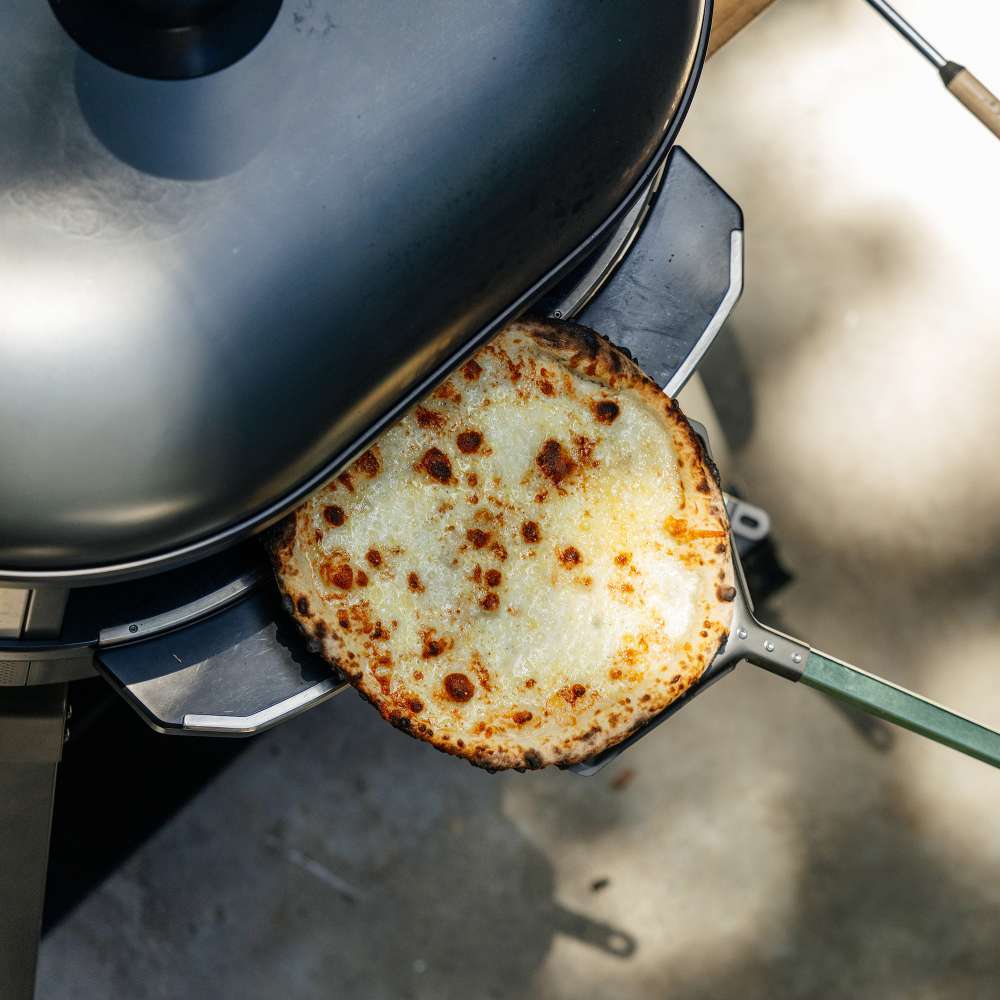 Gozney Dome 2 Mantel seen from above holding a skillet of browned flatbread at the mouth of a gray Dome oven outdoors.