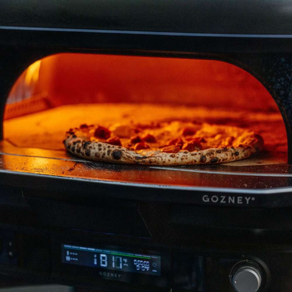 Gozney Dome Gen 2 Natural Gas Pizza Oven close view of a leopard-spotted pizza baking on the stone floor inside the glowing dome with the lit control panel below.
