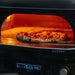 Gozney Dome Gen 2 Natural Gas Pizza Oven close view of a leopard-spotted pizza baking on the stone floor inside the glowing dome with the lit control panel below.