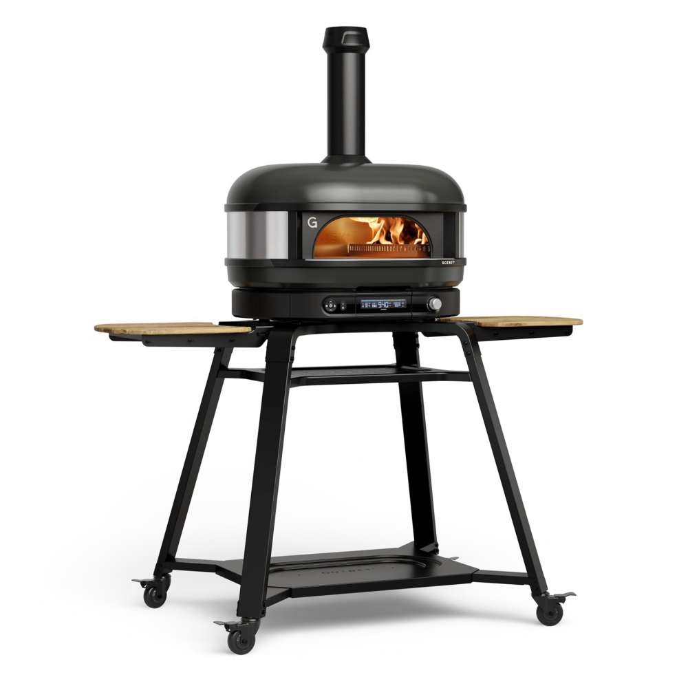 Gozney Dome Gen 2 Natural Gas Pizza Oven on white on its rolling stand with wooden side shelves and casters a flame inside the dome and the chimney fitted on top.