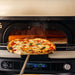 Gozney Neopolitan Arch in place at the mouth of a Bone oven as a finished pizza is drawn out on a peel with steam rising.