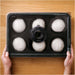 Gozney Pizza Dough Tray held in two hands over a wooden table with six white dough balls resting under the clear lid.