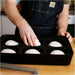 Gozney Pizza Dough Tray on a wooden countertop with a person in a denim apron setting a ball of dough into one of the six wells.