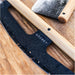 Gozney Pizza Rocker close view of the black curved blade and light wood handle resting on a floured wooden board with the Gozney wordmark on the blade.