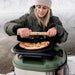Gozney Tread Roof Rack used as a cutting surface by a woman in a beanie and green parka slicing a pizza on top of an Olive Tread oven in the snow.