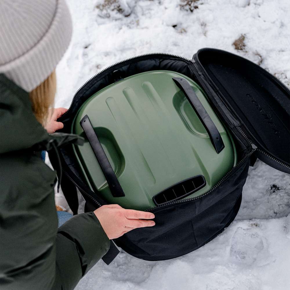 Gozney Tread Travel Bag open on snowy ground as a person in a green parka lifts an Olive Tread oven out of it.