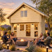 Grand Loft 107 Deluxe DD transformed into a warmly illuminated backyard bar at golden hour. Four adults socialize around a fire feature amid upscale Nevada desert landscaping and distant mountain views.