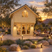 Two-story light wood loft with glass doors and windows, set in a desert landscape with people sitting by a fire pit.