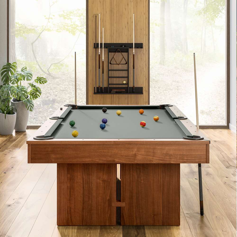 Grey Crate & Barrel Walnut Pool Table with Wall Rack and Accessories seen end on in a room with floor to ceiling windows onto woodland, coloured balls on the grey felt and a cue rack on the wall behind