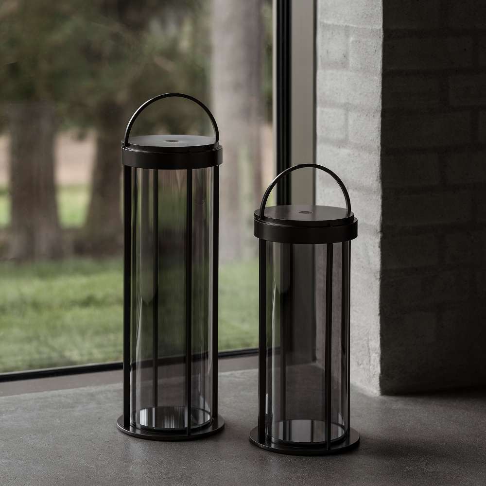 Gunmetal Crate & Barrel Blomus Mituro Rechargeable LED Indoor/Outdoor Lantern shown in a styled setting, a cylindrical tower lamp with a darkened glass shade