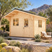 Front-right view of the 107-square-foot Harvest Grand Bungalow Freedom Office Studio in a sunny Nevada backyard. An adult works inside the compact office, surrounded by desert plants, boulders, a lounge chair, and distant mountains.
