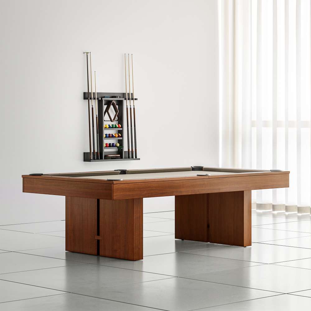 Khaki Crate & Barrel Walnut Pool Table with Wall Rack and Accessories in a bright white tiled room with sheer curtains, khaki felt and a wall cue rack holding cues and balls behind