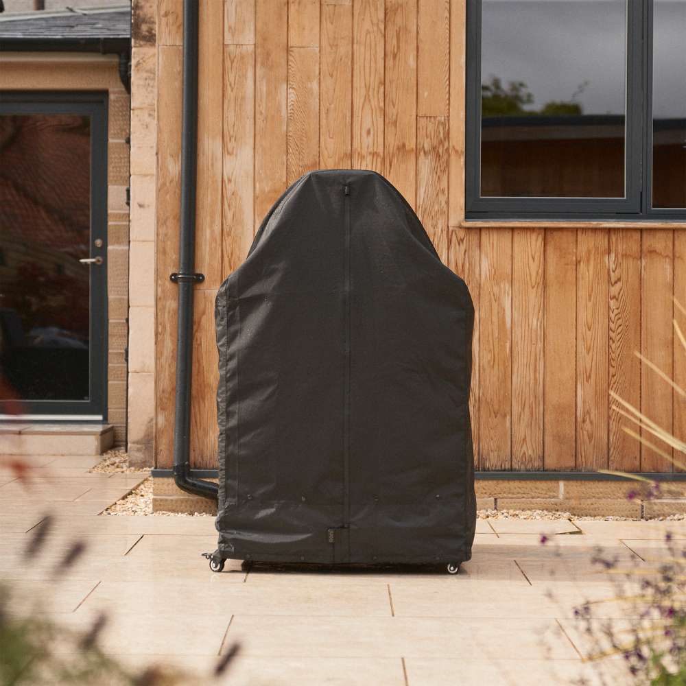 Large Ooni Table and Pizza Oven Cover standing tall over a table on a patio beside a timber clad house with a glass door.