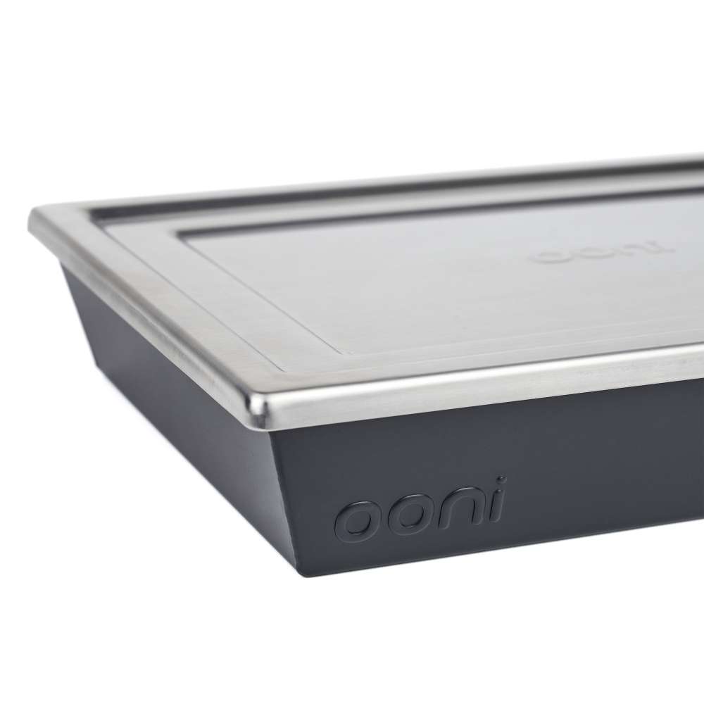 Medium Ooni Detroit Pizza Pan close-up of one corner with the brushed stainless steel lid overhanging the dark gray pan and the ooni logo below.