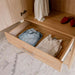 Natural Oak Inovabed Wall Bed with Sofa and Wide Flex Cabinet in close-up with a Wide Flex Cabinet drawer pulled open on folded clothes, red shoes and hanging garments visible above