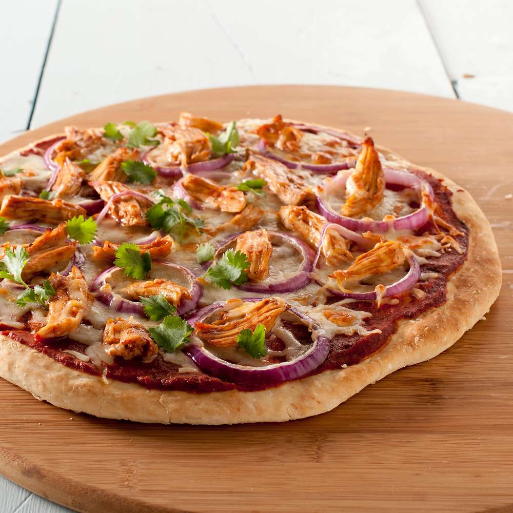 Nordic Ware Naturals 14" Deep Dish Pizza Pan lifestyle shot of a barbecue chicken pizza with red onion and cilantro resting on a round wooden board on a white table.