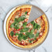 Nordic Ware Naturals 16" Air Crisper Pizza Pan from above on white marble holding a baked tomato and basil pizza with one slice cut away to show the perforated base.