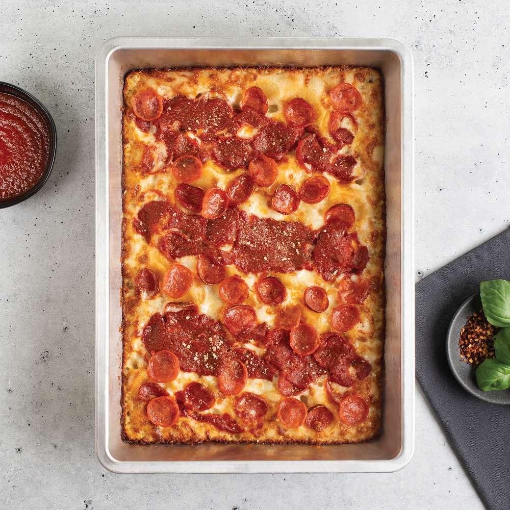 Nordic Ware Naturals Detroit-Style Pizza Pan from above on a gray counter holding a baked pepperoni Detroit-style pizza with a bowl of sauce and a dish of basil and chili flakes alongside.