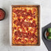 Nordic Ware Naturals Detroit-Style Pizza Pan from above on a gray counter holding a baked pepperoni Detroit-style pizza with a bowl of sauce and a dish of basil and chili flakes alongside.