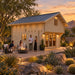 Opposite-side view of the Northwood Grand DD 70mm Freedom Loft Studio at golden hour. Four adults socialize around a fire feature while the illuminated backyard bar is visible through the double glass doors.
